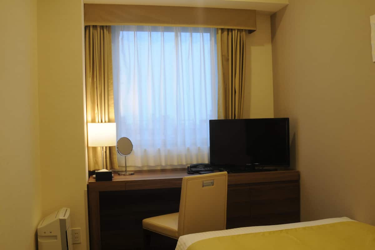 Une chambre d’hôtel comprenant un lit, un bureau avec une télévision, une lampe et un téléphone.