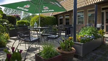 An outdoor patio area with a table and chairs, a green umbrella, and potted plants.