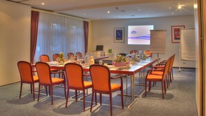 Un salón de conferencias con una larga mesa, múltiples sillas, una pantalla de proyector y una pizarra.
