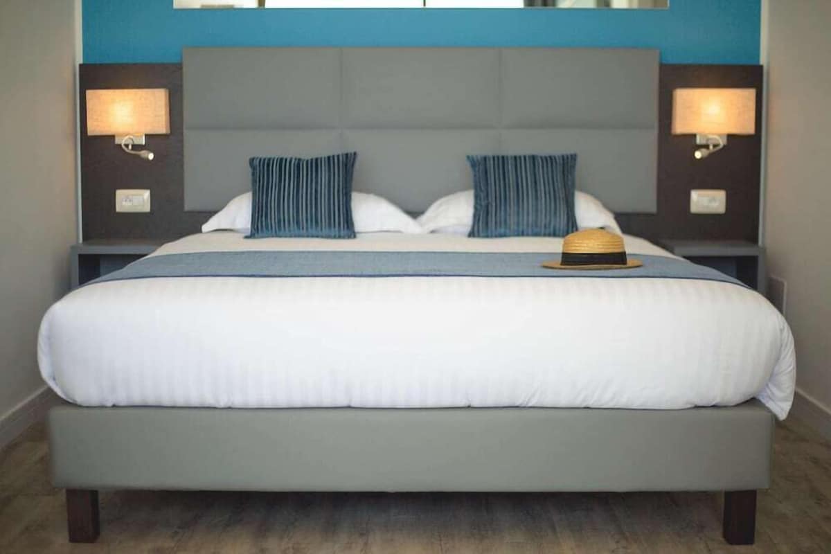 A large bed with a grey headboard, two bedside lamps, and a blue-striped pillow.