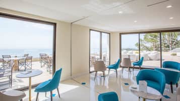 A modern lounge area with a view of the sea, featuring blue chairs, a small table, and a glass partition.