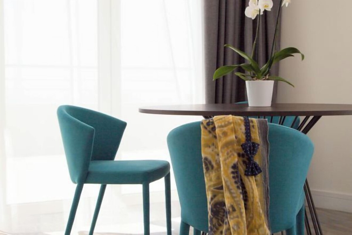 A dining area with a table and two chairs, a potted plant, and a window with curtains.