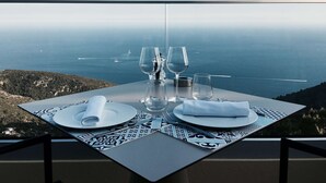 A table set for two with a view of the ocean and hills in the background. - Hôtel Les Terrasses D'Eze (Èze)