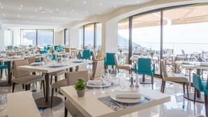 A modern restaurant with tables set for dining, large windows offering a view of the mountains, and a clean, contemporary interior design. - Hôtel Les Terrasses D'Eze (Èze)