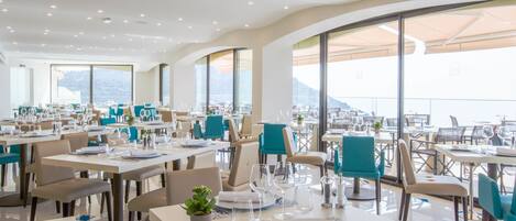 A modern restaurant with tables set for dining, large windows offering a view of the mountains, and a clean, contemporary interior design.