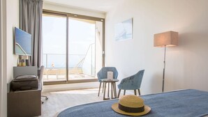 A hotel room with a bed, a desk, a chair, a small table, and a balcony with a view. - Hôtel Les Terrasses D'Eze (Èze)
