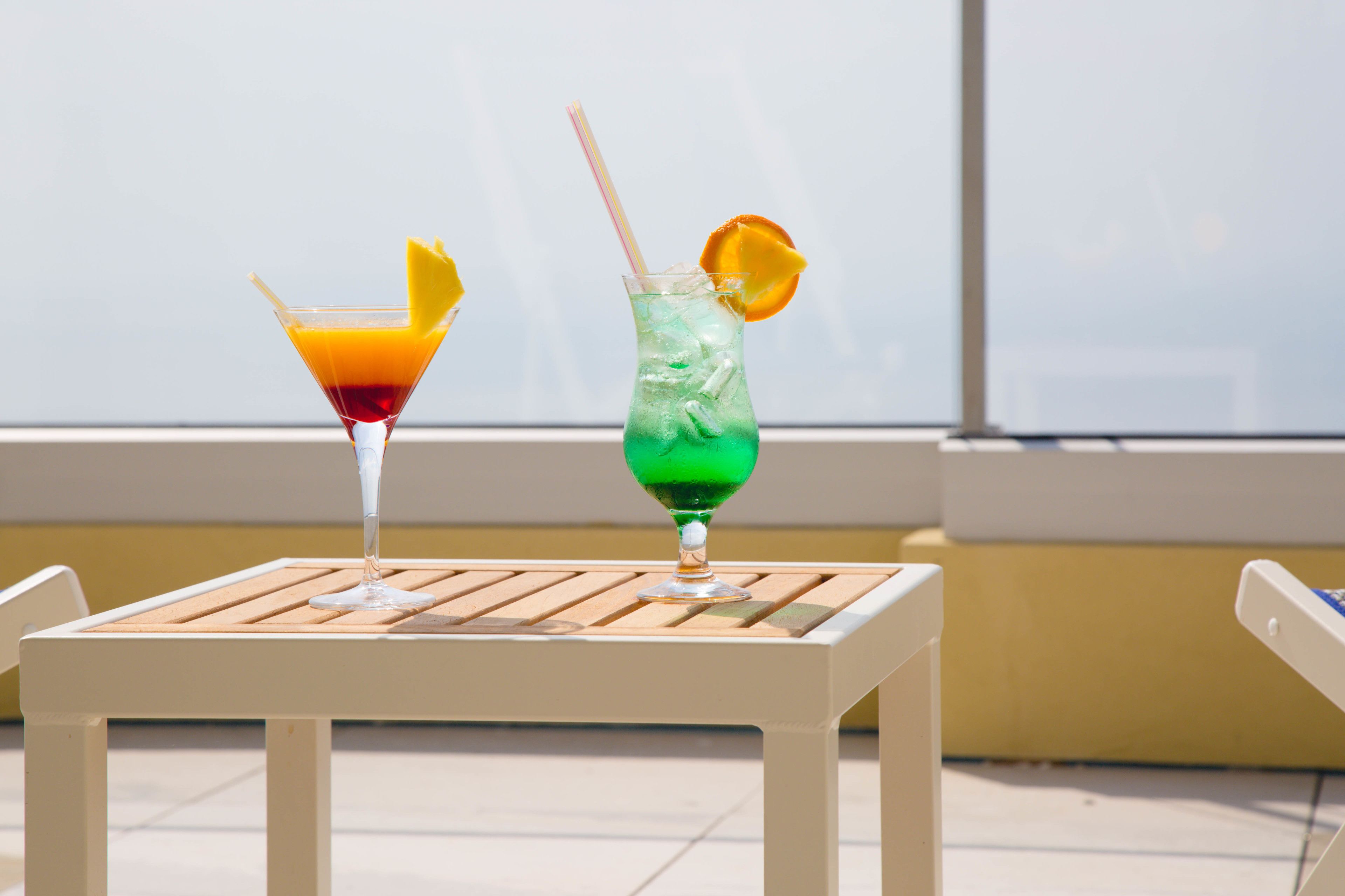Two cocktails on a white table with a window in the background.