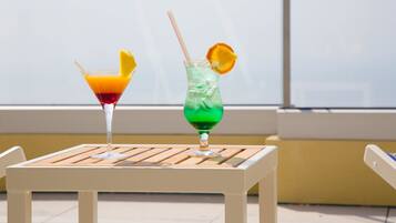 Two cocktails on a white table with a window in the background.