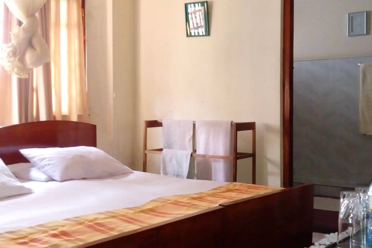 Une chambre d’hôtel avec un lit, un bureau en bois doté d’un miroir et une fenêtre avec des rideaux.