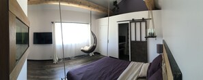 A bedroom with a bed, a hanging chair, a large mirror, and a TV on the wall. - La Datcha Delicatessen (Tulette)