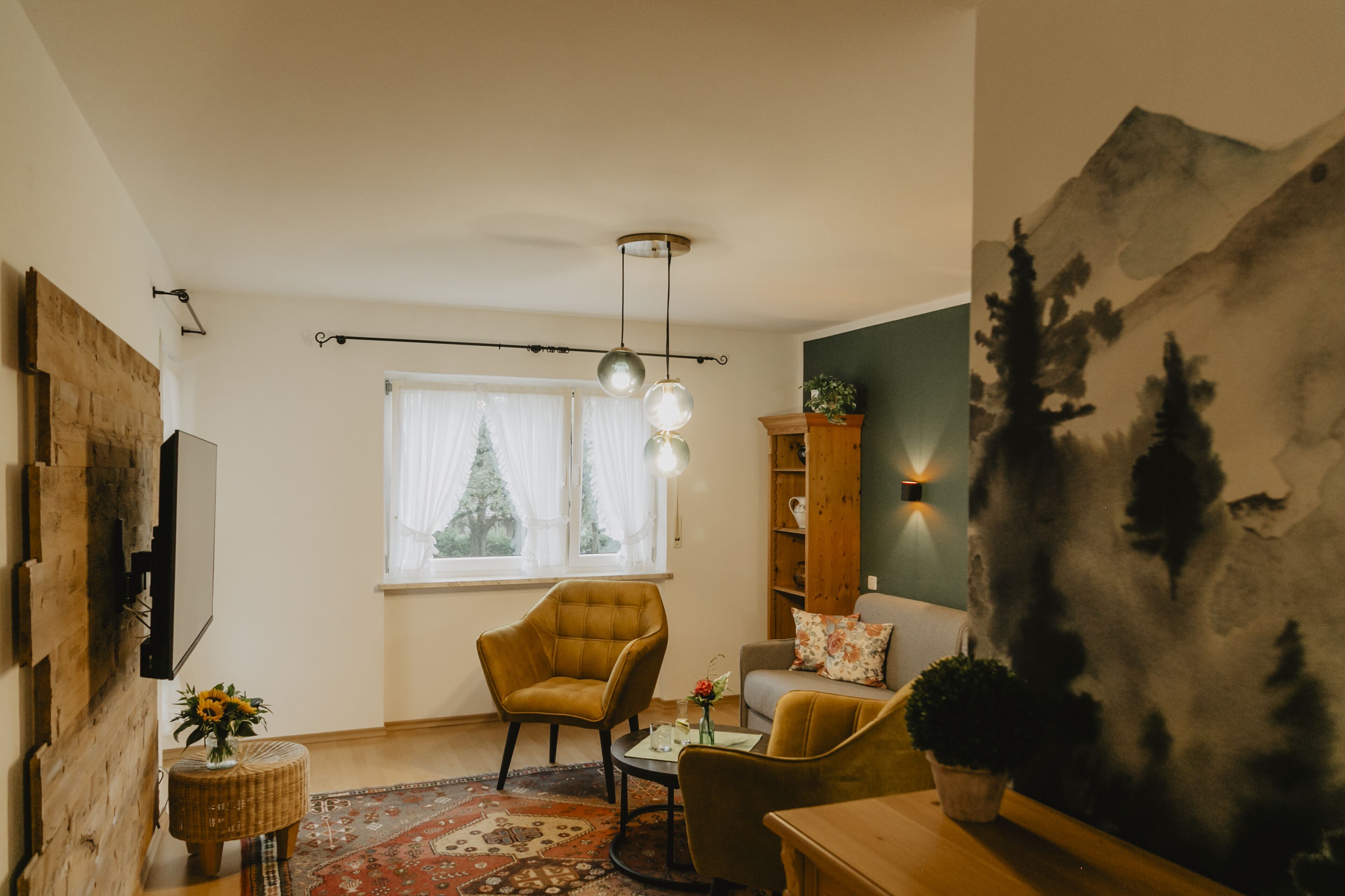 A living room with a sofa, armchair, and a coffee table. There is a window with curtains, a wall-mounted shelf, and a painting.
