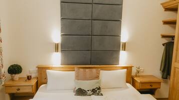 A neatly arranged hotel room with a large bed, two bedside tables, a nightstand, a wooden headboard with built-in lighting, and a small potted plant.