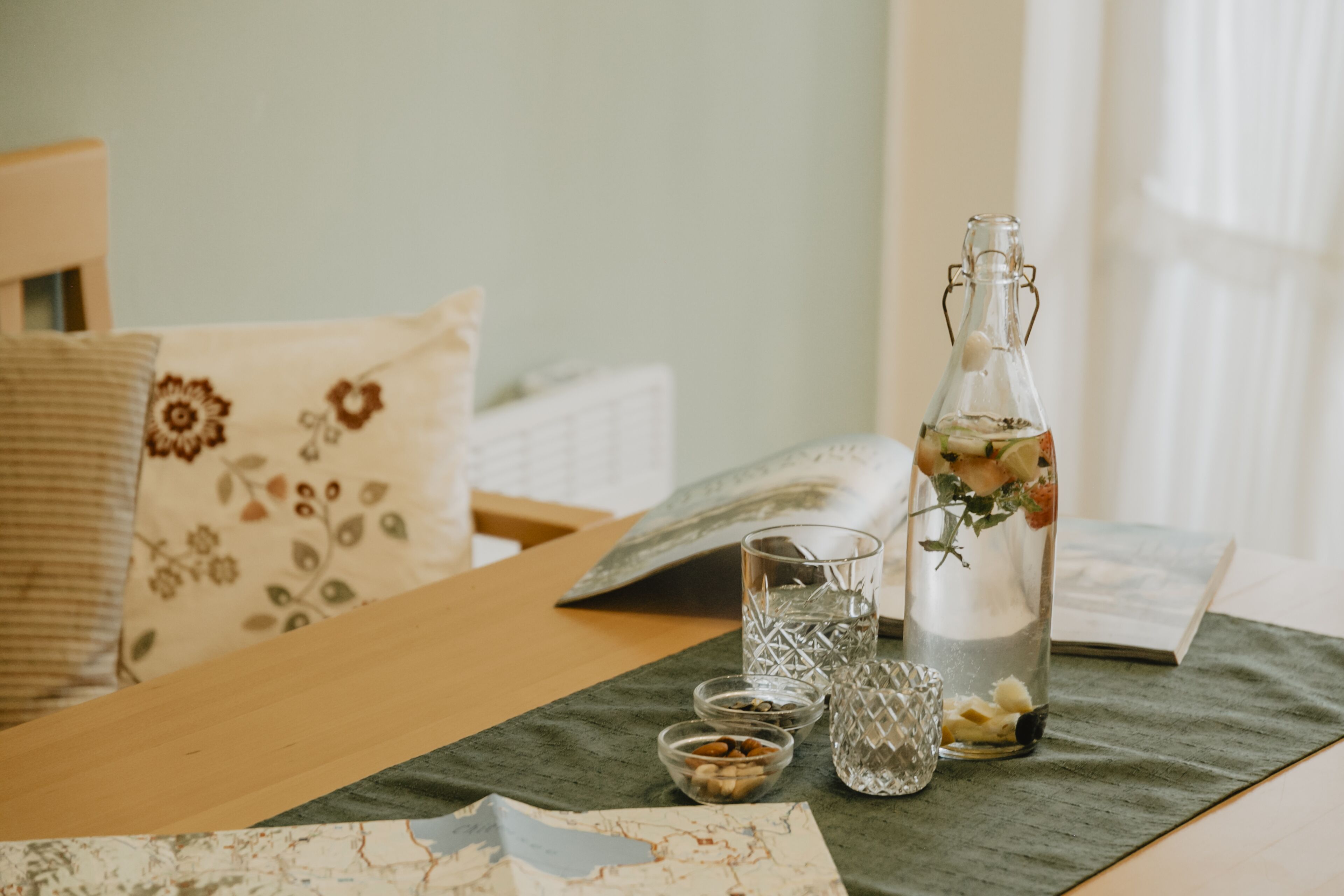 A neatly arranged bedroom with a bed, pillows, a bedside table with a book, a bottle, and glasses.