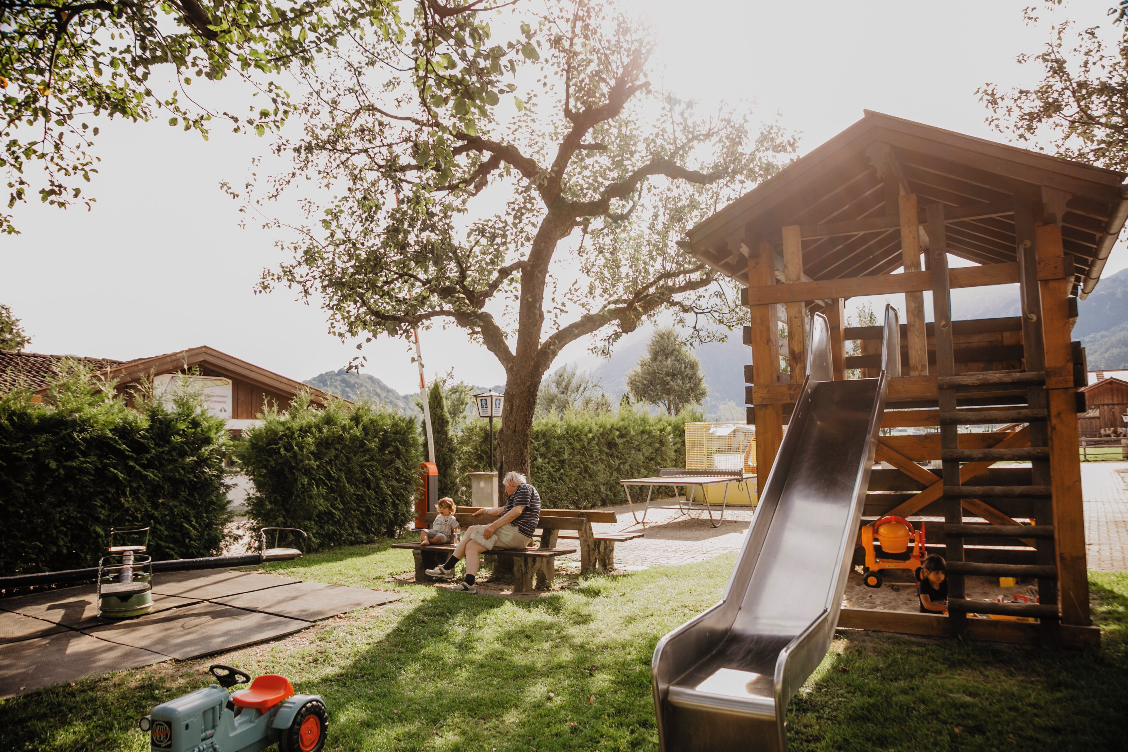 Une structure de jeu en bois avec un toboggan, une table de pique-nique et un tracteur, installée dans un jardin.