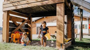 A wooden structure with a covered entrance, a child holding a bucket, and another child playing with toys.