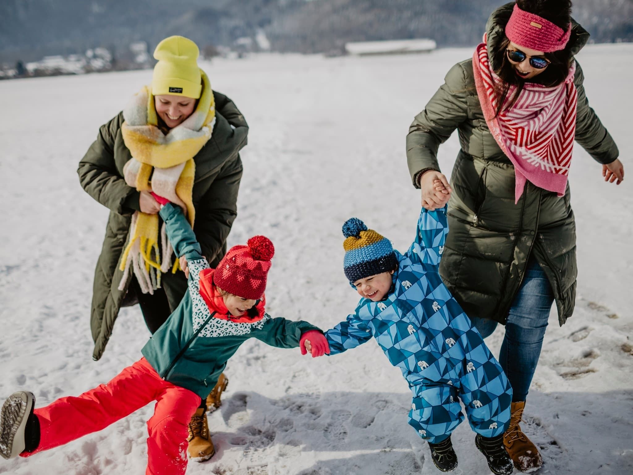 A family of four in a snowy outdoor setting, holding hands and walking together.