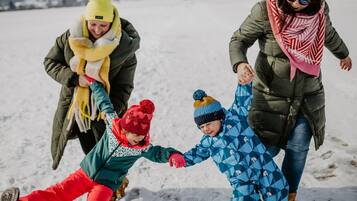 A family of four in a snowy outdoor setting, holding hands and walking together.
