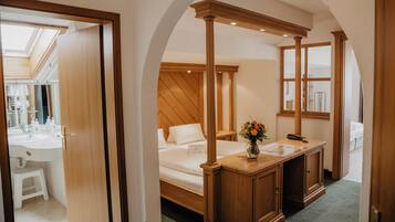 A hotel room with a wooden bed, a small desk, a mirror, and a view of the bathroom.