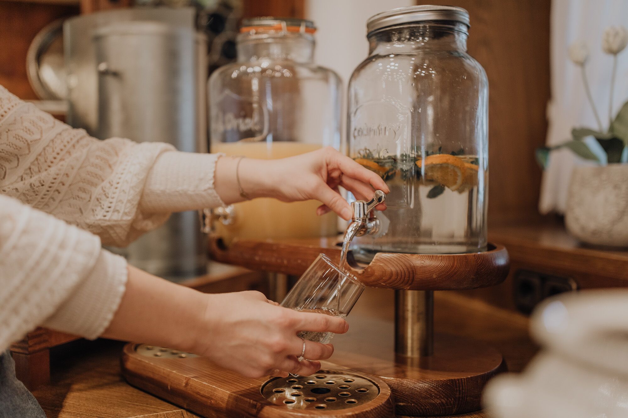 A person pouring water from a tap into a glass on a wooden table.