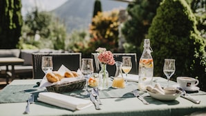 Mesa de comedor al aire libre con comida, bebidas y un florero.