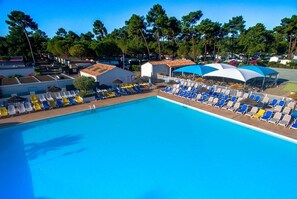 A swimming pool with sun loungers and umbrellas, surrounded by trees and buildings. - Camping La Palmyre Estanquet (Les Mathes)