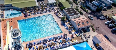 An aerial view of a resort with a large swimming pool, sun loungers, and a water slide.