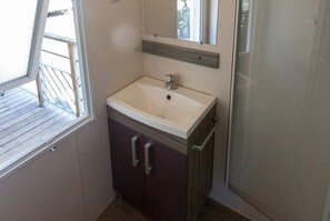 A bathroom with a white sink, dark cabinets, a mirror, and a window. - Camping La Palmyre Estanquet (Les Mathes)