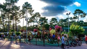Ein Spielplatz mit Rutschen und Klettergerüsten, umgeben von Bäumen und einem Zaun.