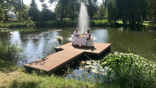 A wooden dock extending into a calm lake with a fountain in the center. - Schloss Diedersdorf (Grossbeeren)