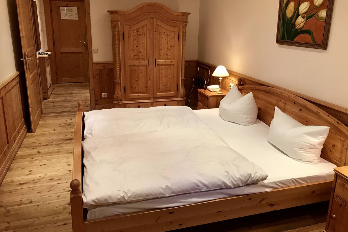 Ein hölzernes Bett mit weißen Leinen, ein Holzschrank, ein Nachttisch mit Lampe und ein Gemälde mit Tulpen an der Wand.