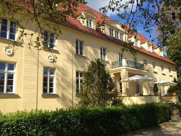 A multi-story building with a red-tiled roof, large windows, and a balcony with outdoor seating. - Schloss Diedersdorf (Grossbeeren)