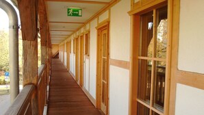 A corridor with wooden railings, large windows, and a green emergency exit sign. - Schloss Diedersdorf (Grossbeeren)