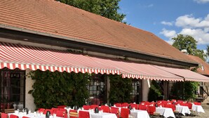 An outdoor dining area with tables set for guests, covered by striped awnings, and a stone-paved ground. - Schloss Diedersdorf (Grossbeeren)