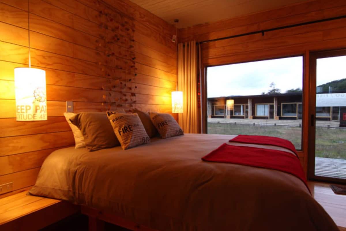 A wooden room with a bed, pillows, and a window.