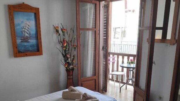 A bedroom with a bed, a painting, a vase with flowers, and a balcony.