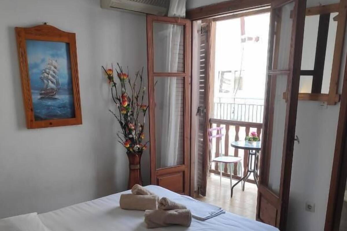 A bedroom with a bed, a painting, a vase with flowers, and a balcony.