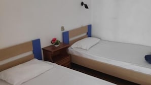 Two single beds with wooden headboards and white bedding, a small bedside table with a lamp, and a wall-mounted light fixture.