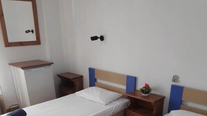 A room with two beds, a small table, a shelf, and a mirror.