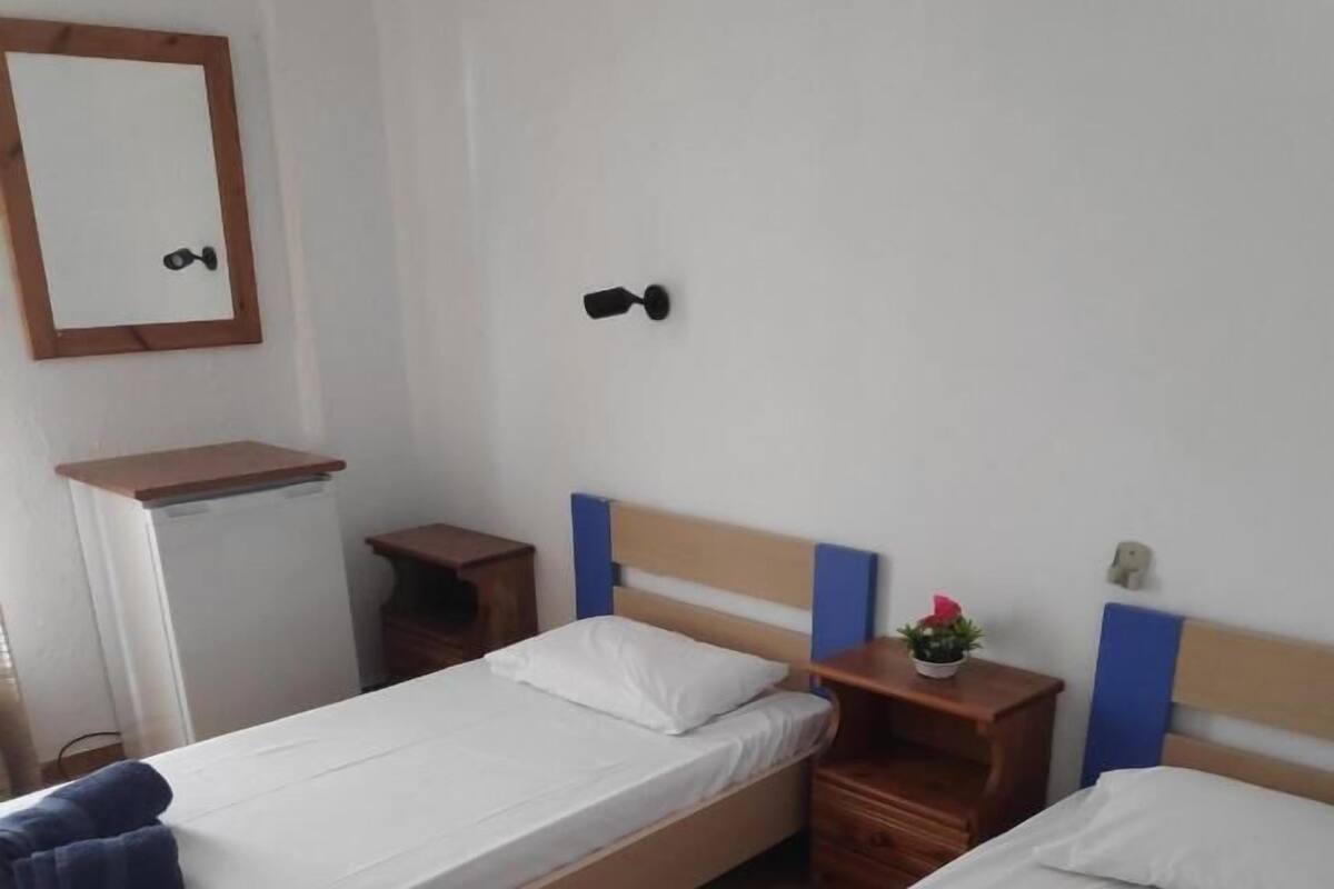 A room with two beds, a small table, a shelf, and a mirror.