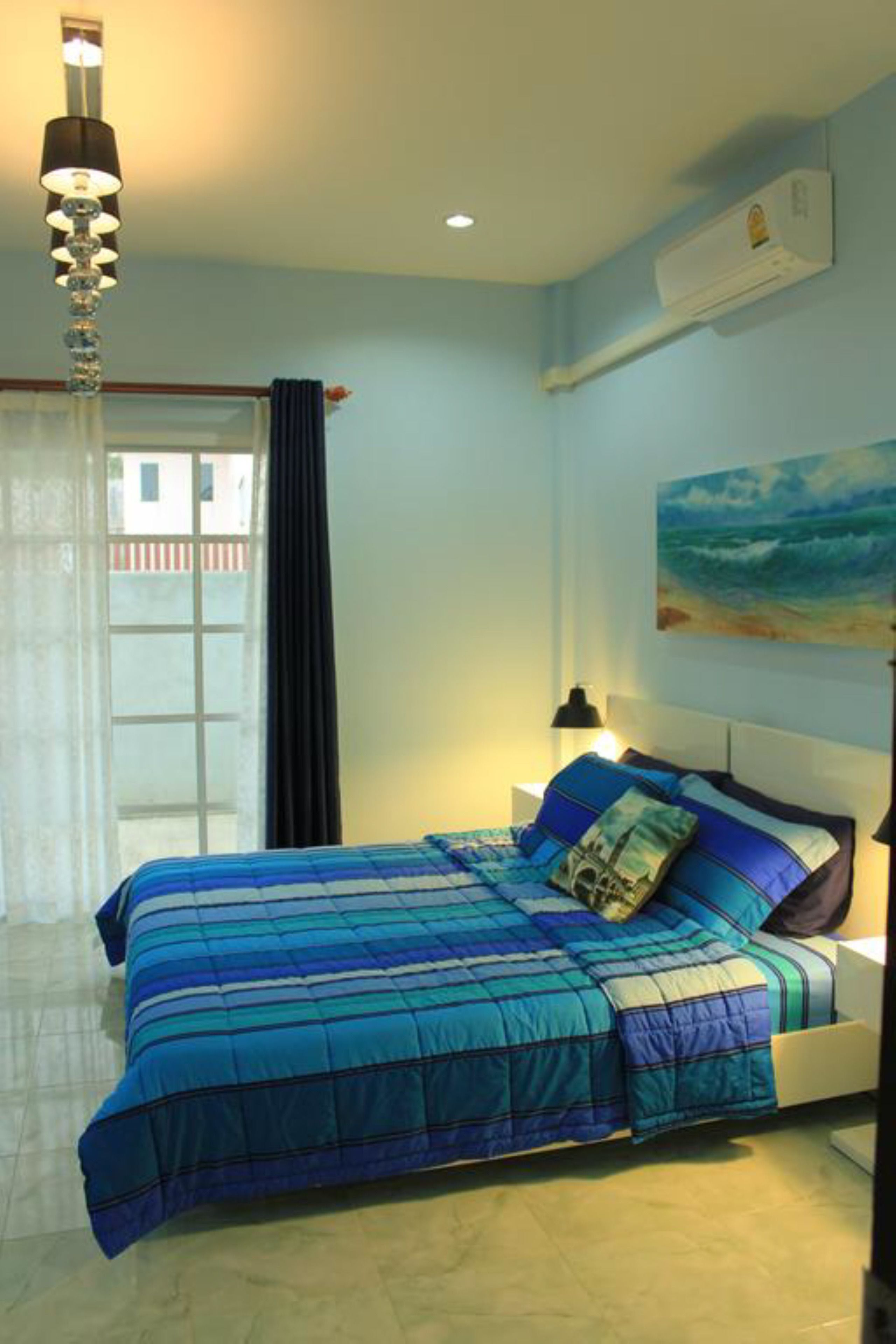 Een slaapkamer met een bed, nachtkastje, lamp, airconditioner en een schilderij aan de muur.