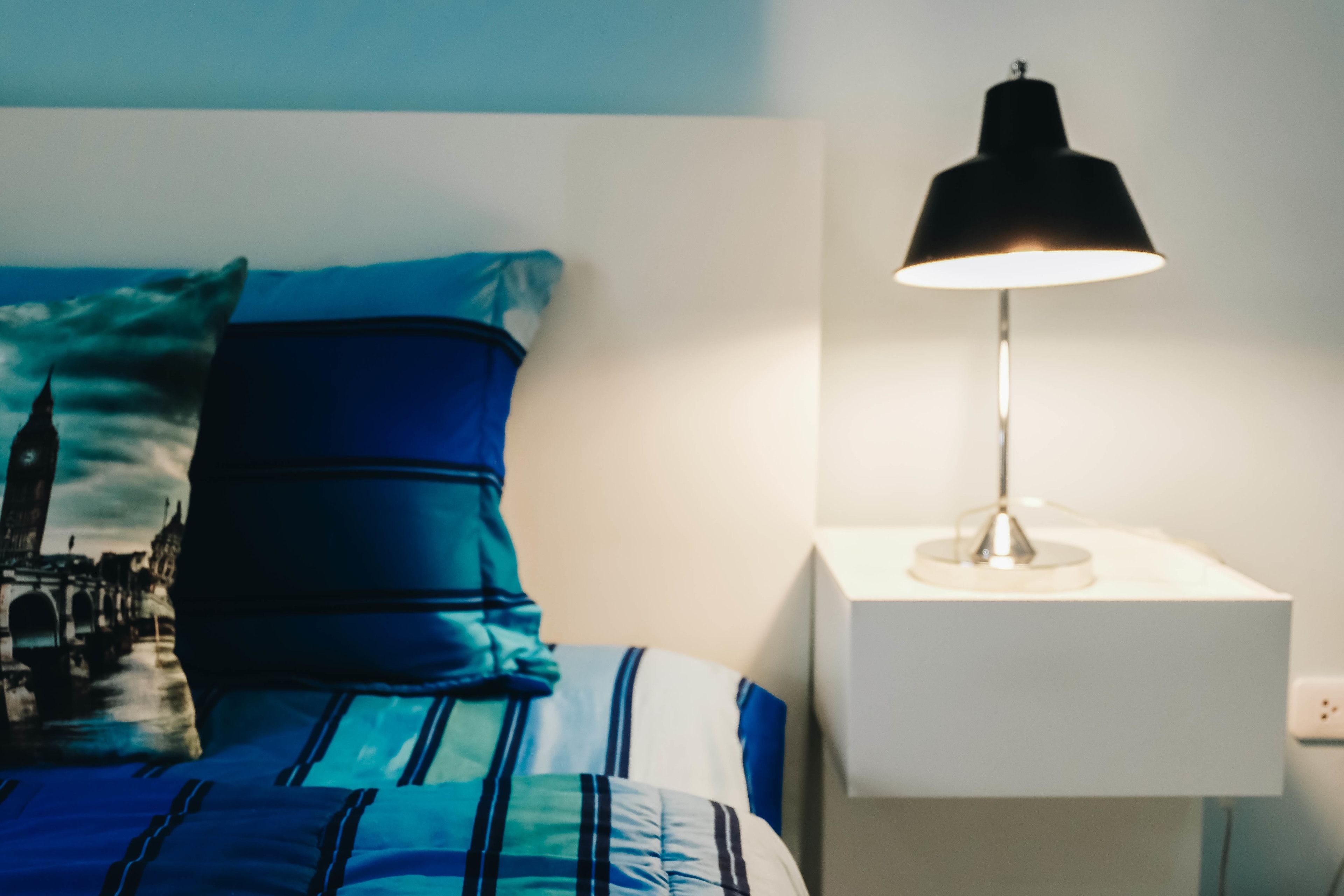 Una cama con ropa de cama azul y una mesita de noche blanca con una lámpara.