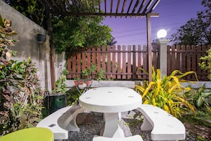 A concrete outdoor seating area with a round table and chairs, surrounded by plants and a wooden fence. - Peach Hua Hin Pool Villa Holiday (Hua Hin)
