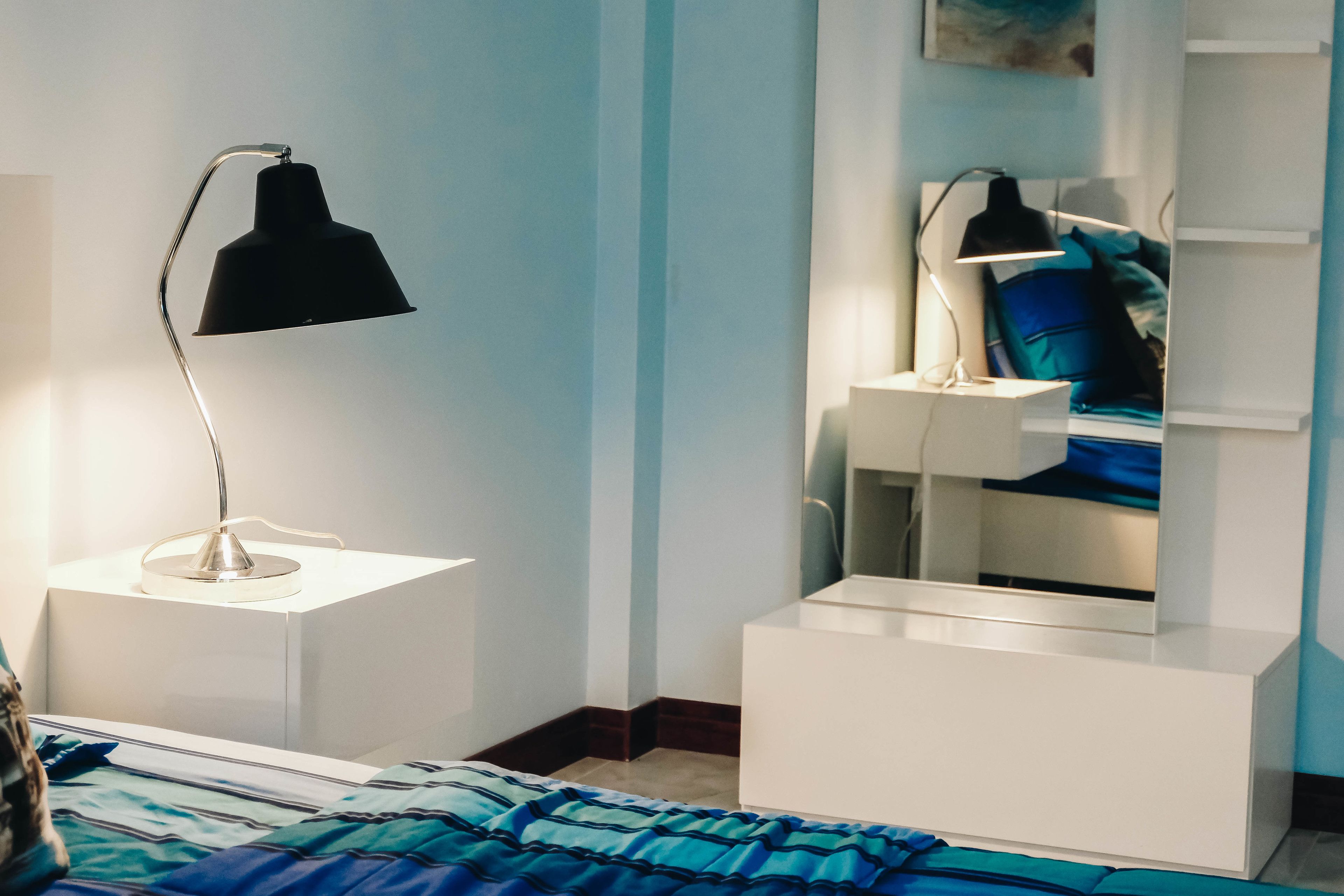 Een slaapkamer met een bed, een nachtkastje met een lamp, een kaptafel en een spiegel.