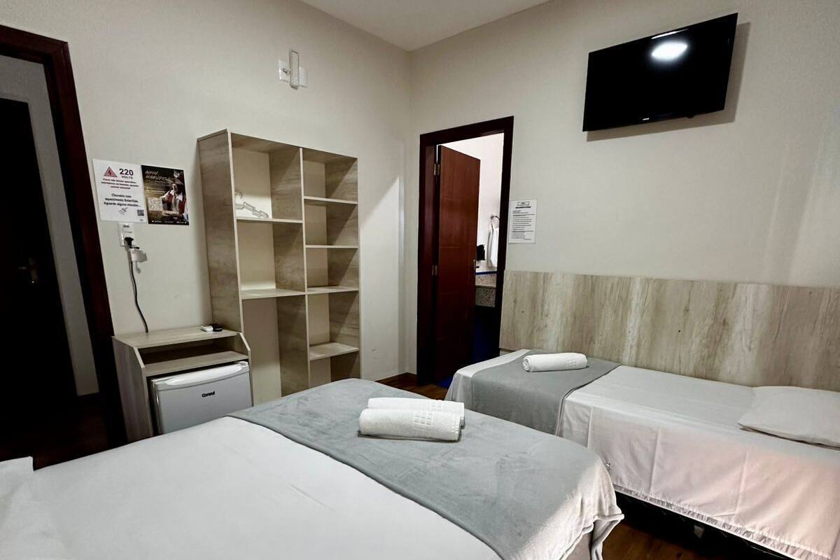 A hotel room with two beds, a TV, a wardrobe, and a desk with a computer.