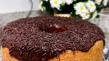 Un pastel bundt bañado en chocolate con grageas sobre un plato de vidrio transparente.