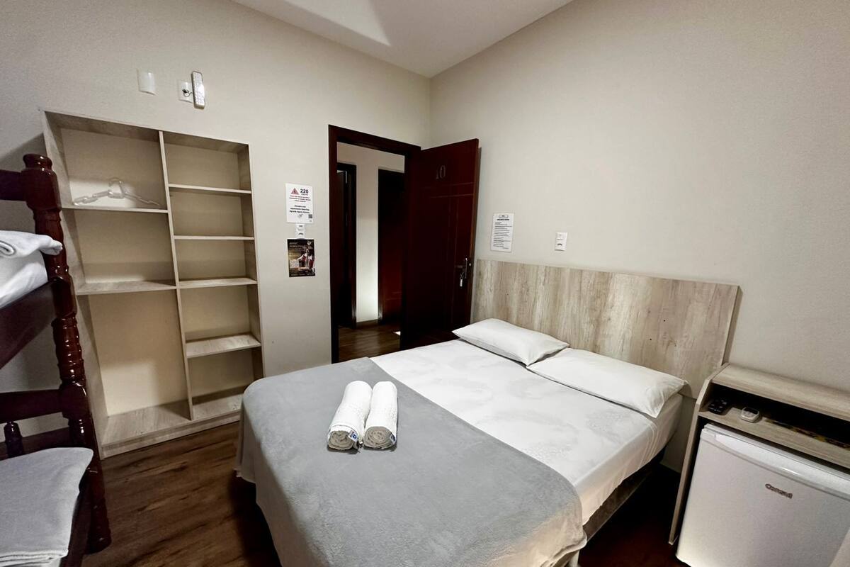 A hotel room with a bed, a wardrobe, a desk with a refrigerator, and a door leading to another room.