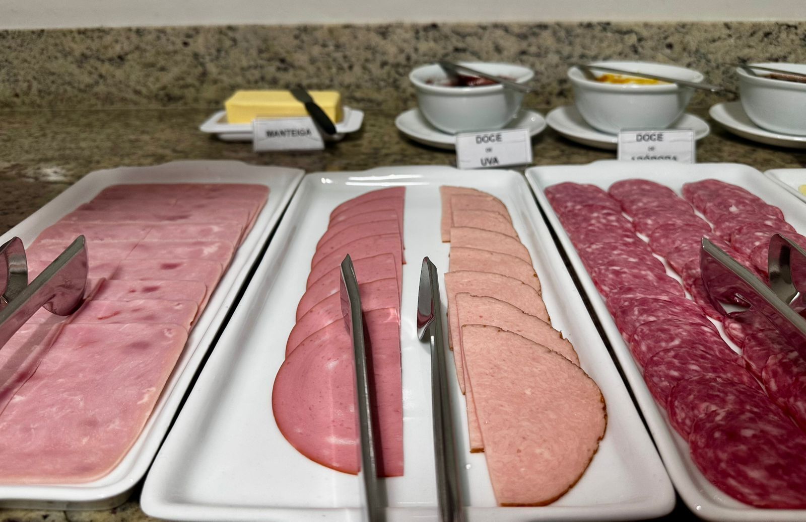 Buffet com diversos tipos de carne, incluindo presunto e salame, expostos em bandejas.