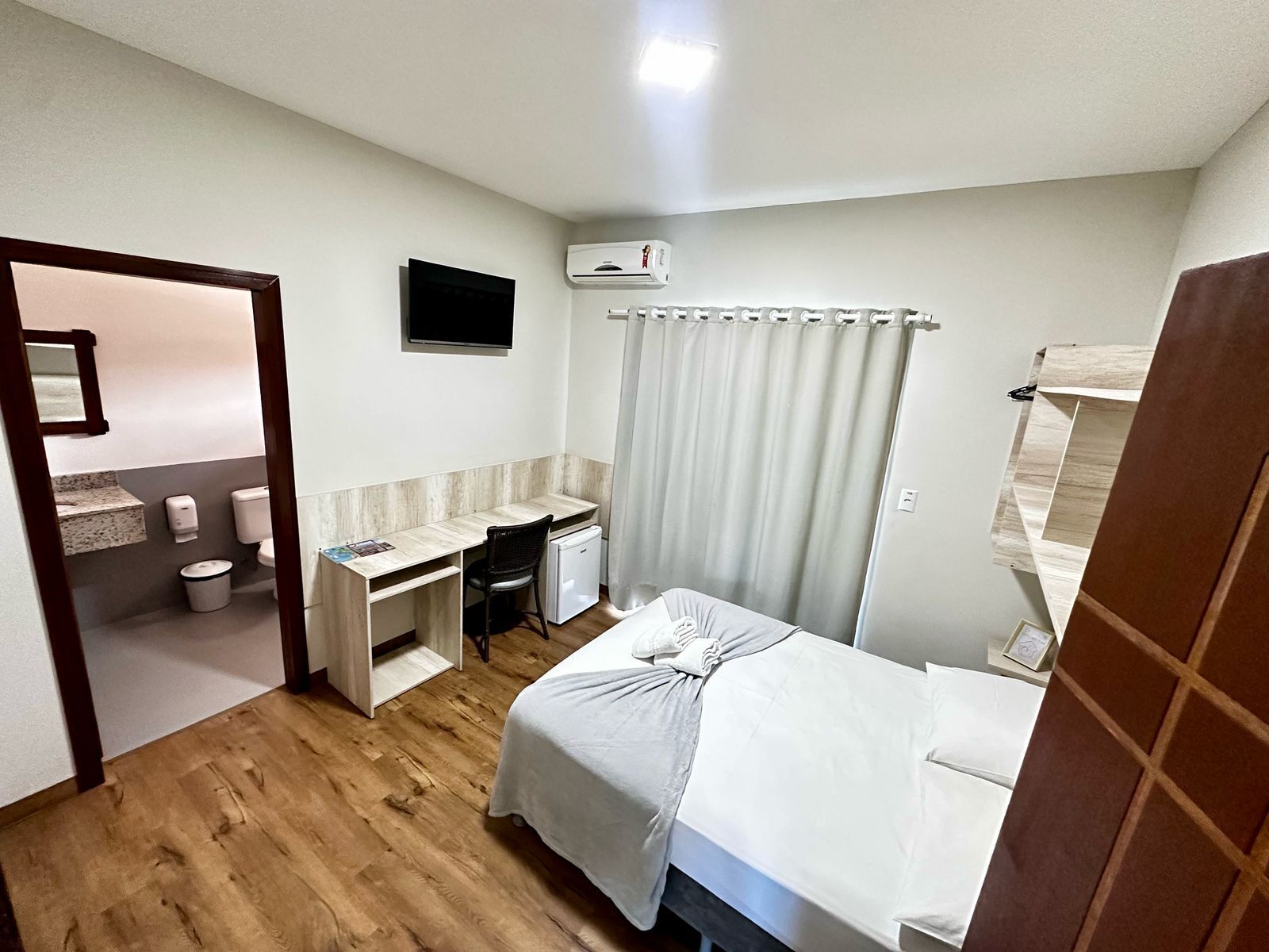 A compact hotel room with a bed, a desk, a chair, a television, and a bathroom.