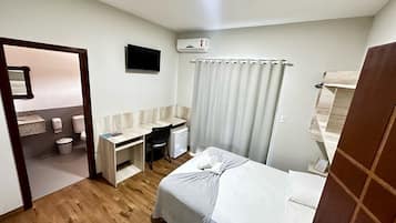 A compact hotel room with a bed, a desk, a chair, a television, and a bathroom.