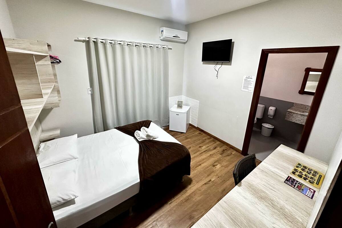 A small, clean room with a bed, a desk, a chair, a toilet, and a shower area.